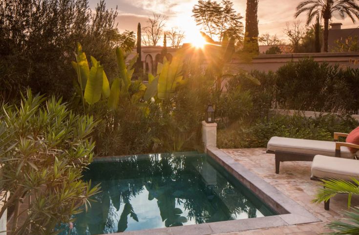 the sun is setting over an outdoor pool with chaise lounges and palm trees