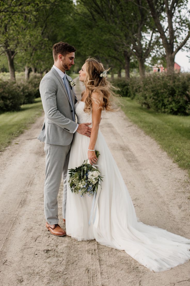 a bride and groom standing in the middle of a dirt road