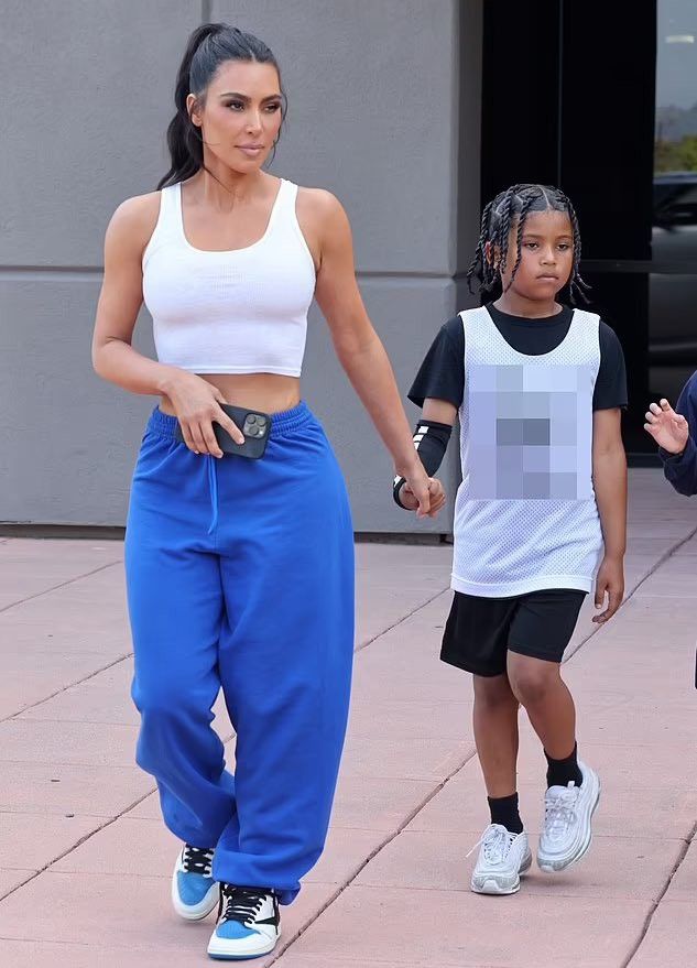 a woman in blue pants and white top walking with two children on the sidewalk,