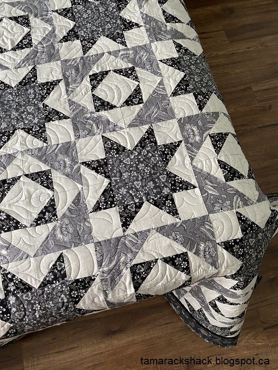 a black and white quilt on top of a bed with wooden floors in the background