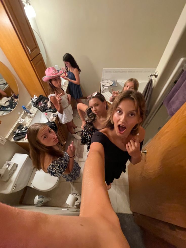 a woman taking a selfie in the bathroom while others look at her and take pictures