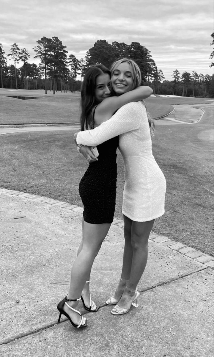 two young women hugging each other on the sidewalk in front of a golf course, black and white photograph