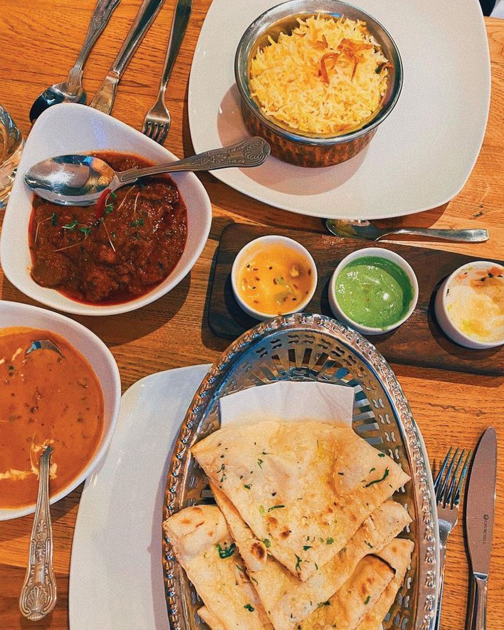 a table topped with plates and bowls filled with different types of food next to silverware