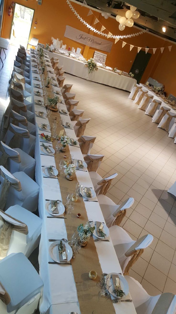 a long table set up with white chairs and place settings for an event or party