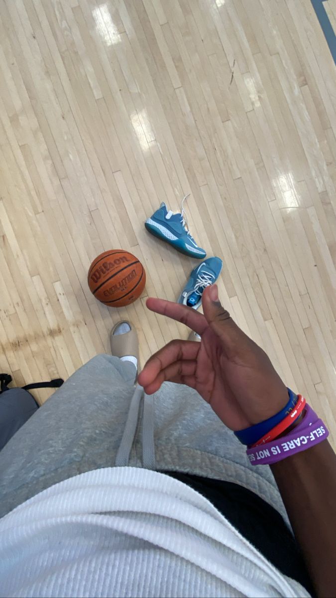 a person sitting on top of a basketball court next to two shoes and a ball