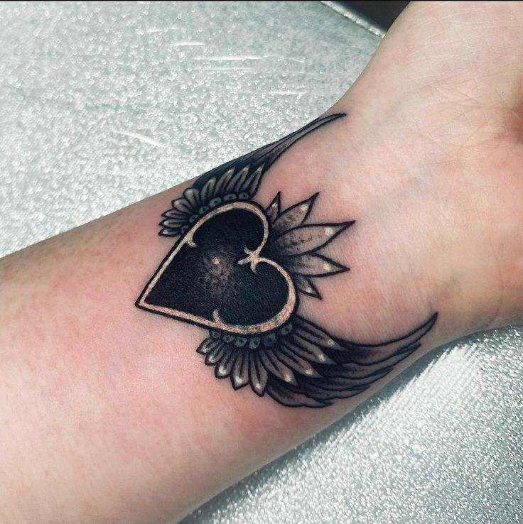 a black and white photo of a heart with wings on the wrist, tattoo style