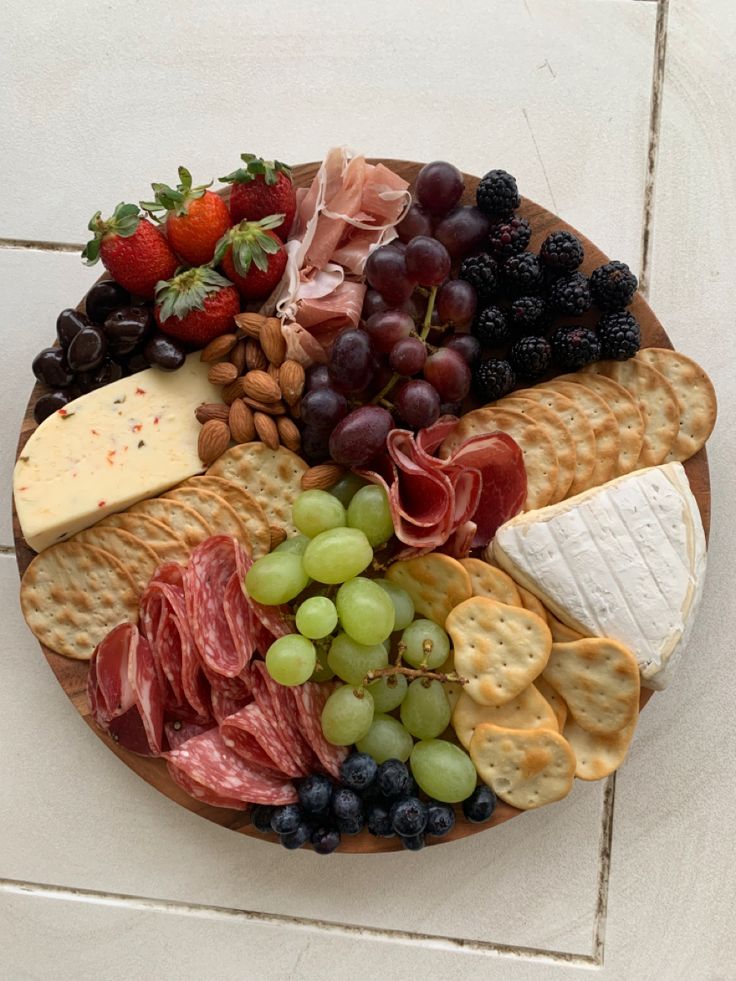 an assortment of cheeses, crackers and grapes on a plate