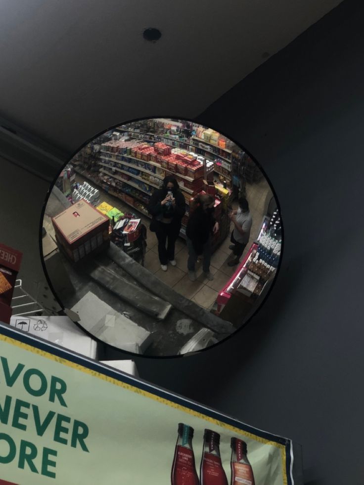 a mirror that is on the side of a wall above a store sign with people in it