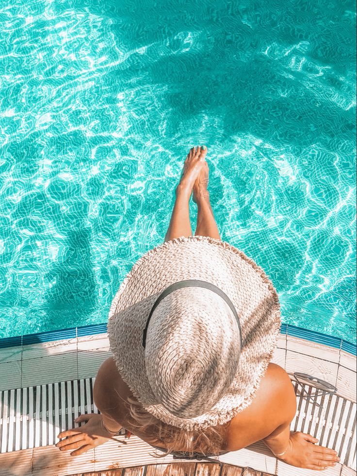 a woman in a straw hat is sitting by the pool with her feet on the edge