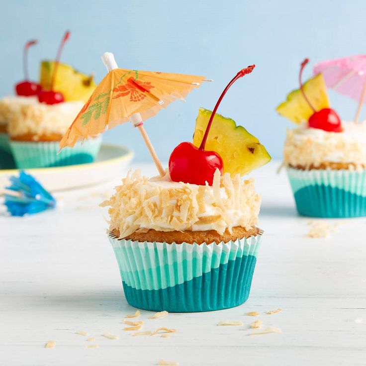 three cupcakes with pineapple, cherries and umbrella toppings on them