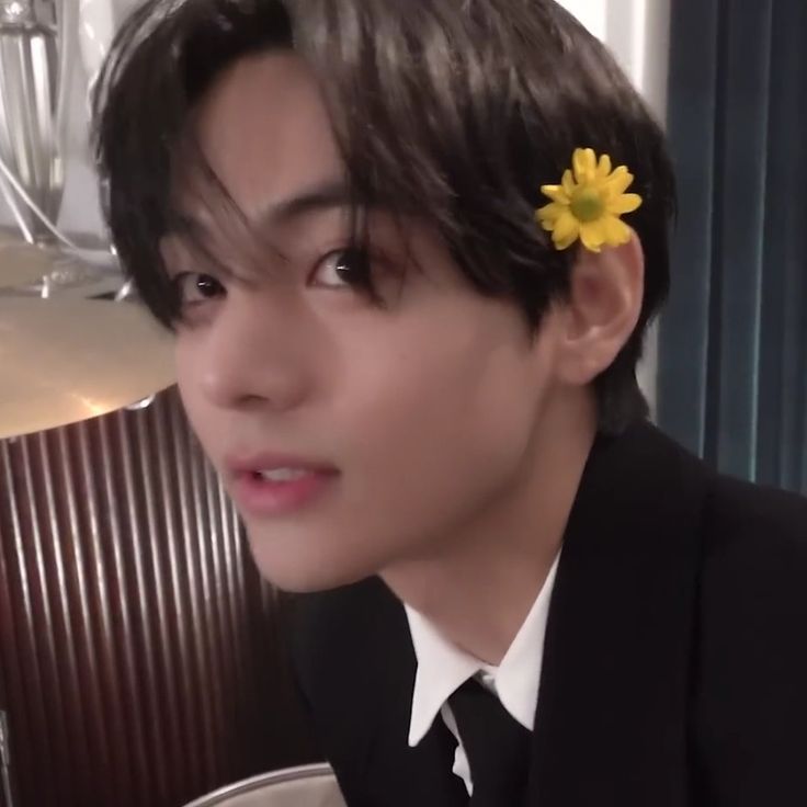 a young man with a flower in his hair sitting at a table and looking off to the side