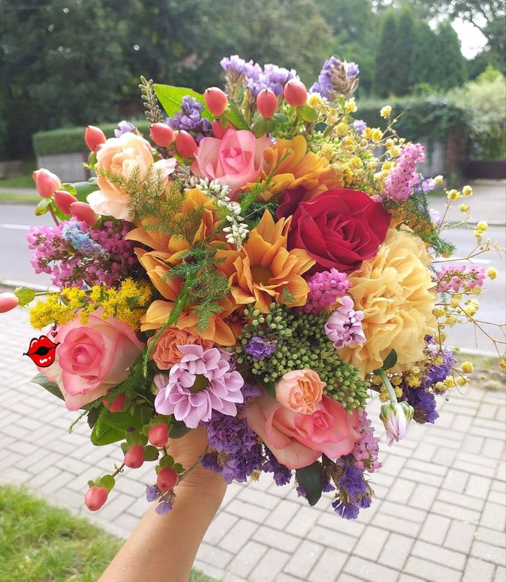 a person holding a bouquet of flowers in their hand on the sidewalk outside with grass and brick walkway behind them