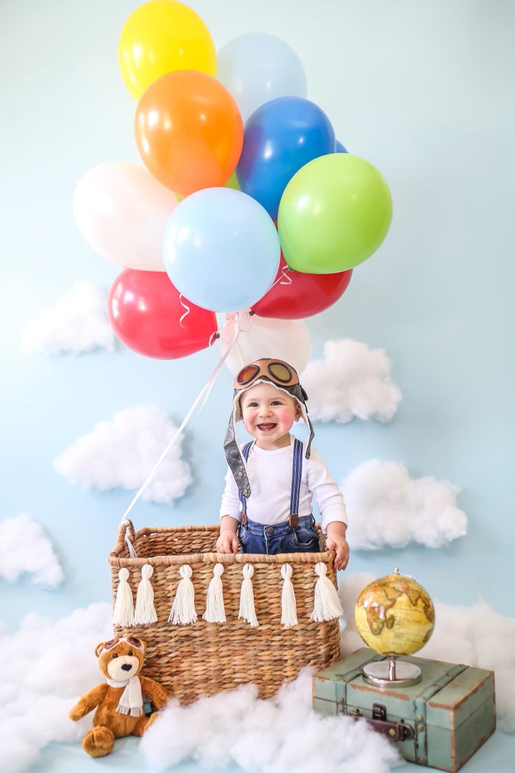 a baby is sitting in a basket with balloons