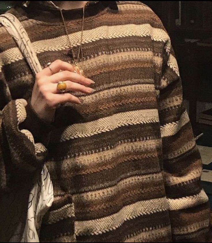 a woman wearing a brown and black striped sweater holding a cell phone in her hand