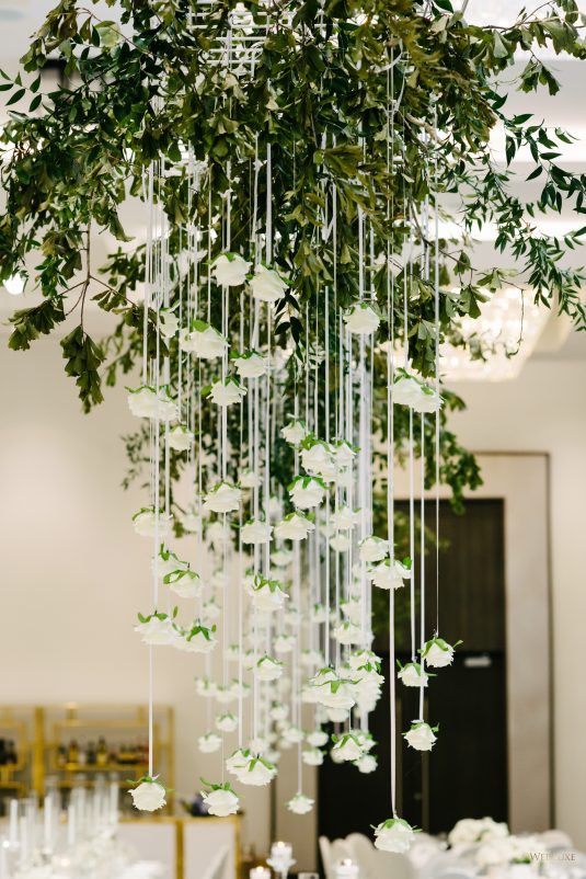 an arrangement of white flowers and greenery hangs from the ceiling in a banquet hall