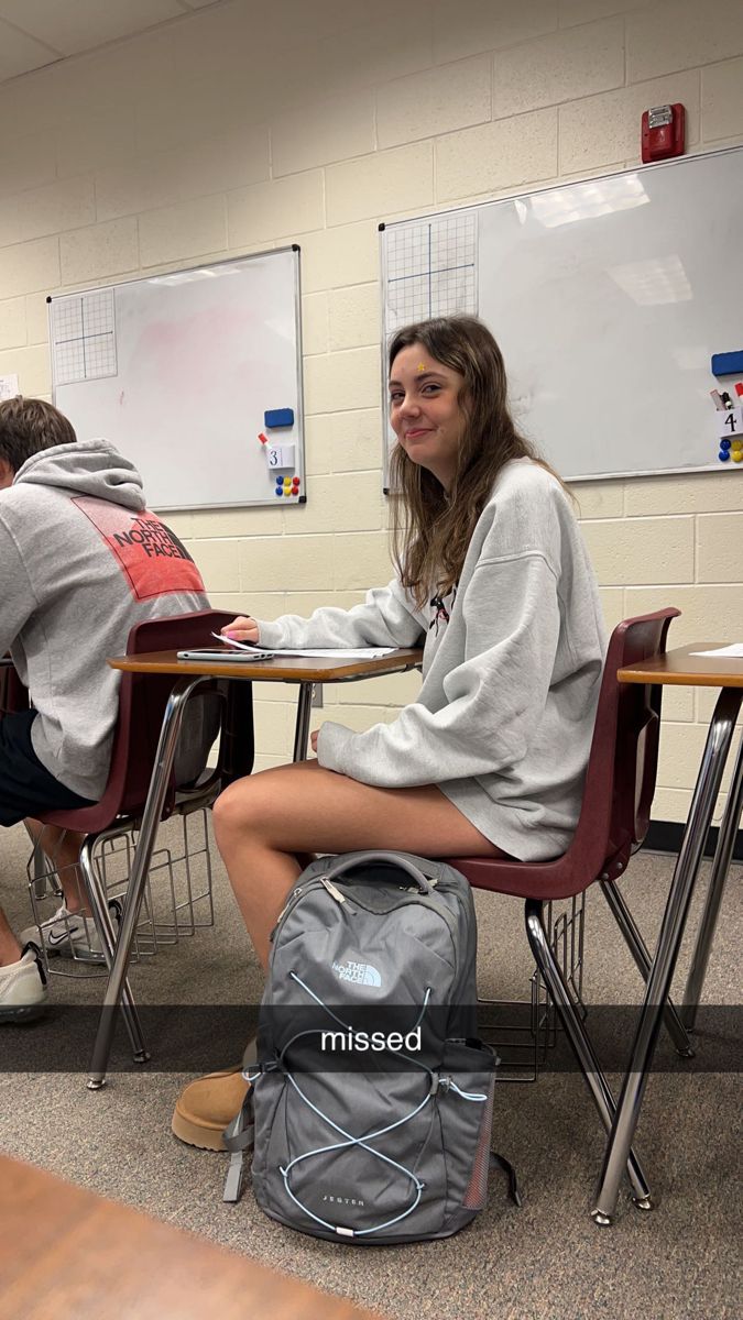 two students sitting at desks with backpacks on the floor in front of them