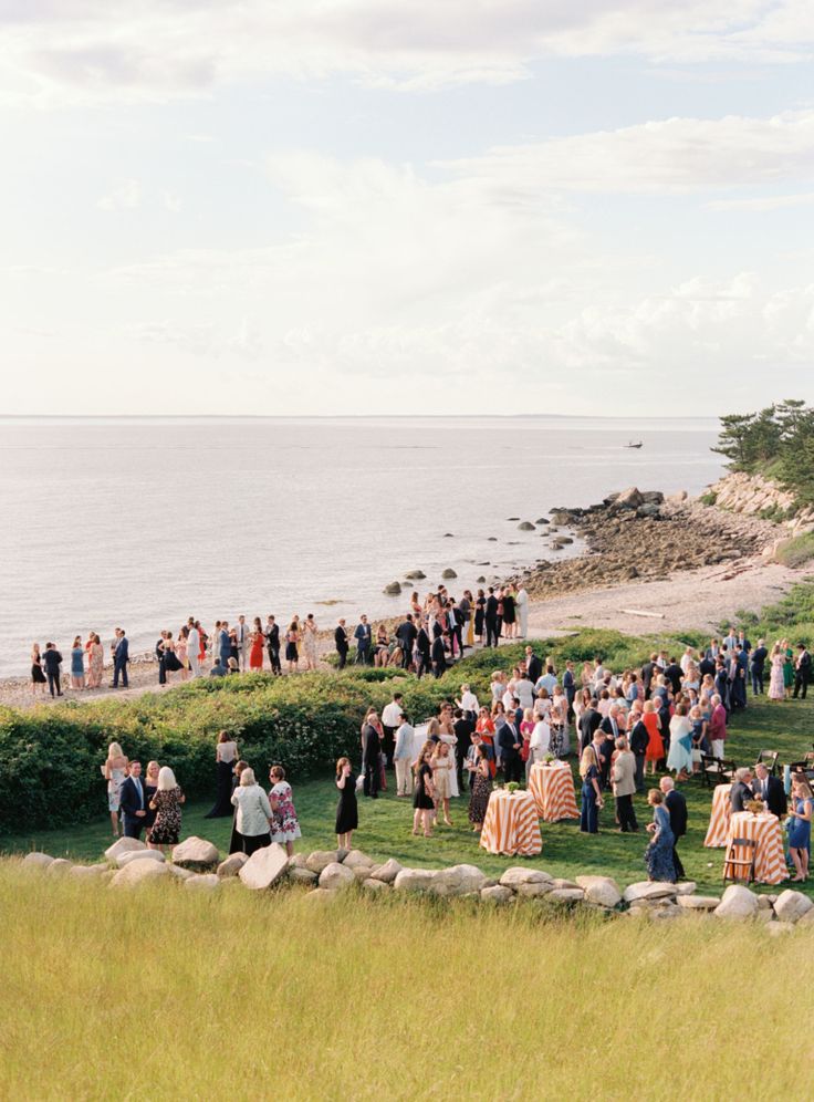 a group of people standing on top of a lush green field next to the ocean