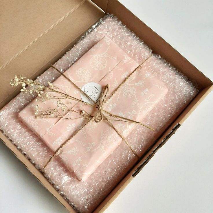 an open box with pink wrapping paper and some dried flowers on the inside, sitting on a white surface