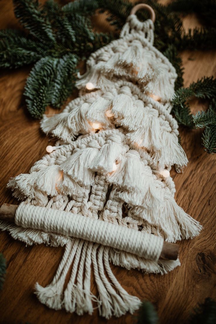 a christmas tree made out of yarn and lights on a wooden table with evergreen branches