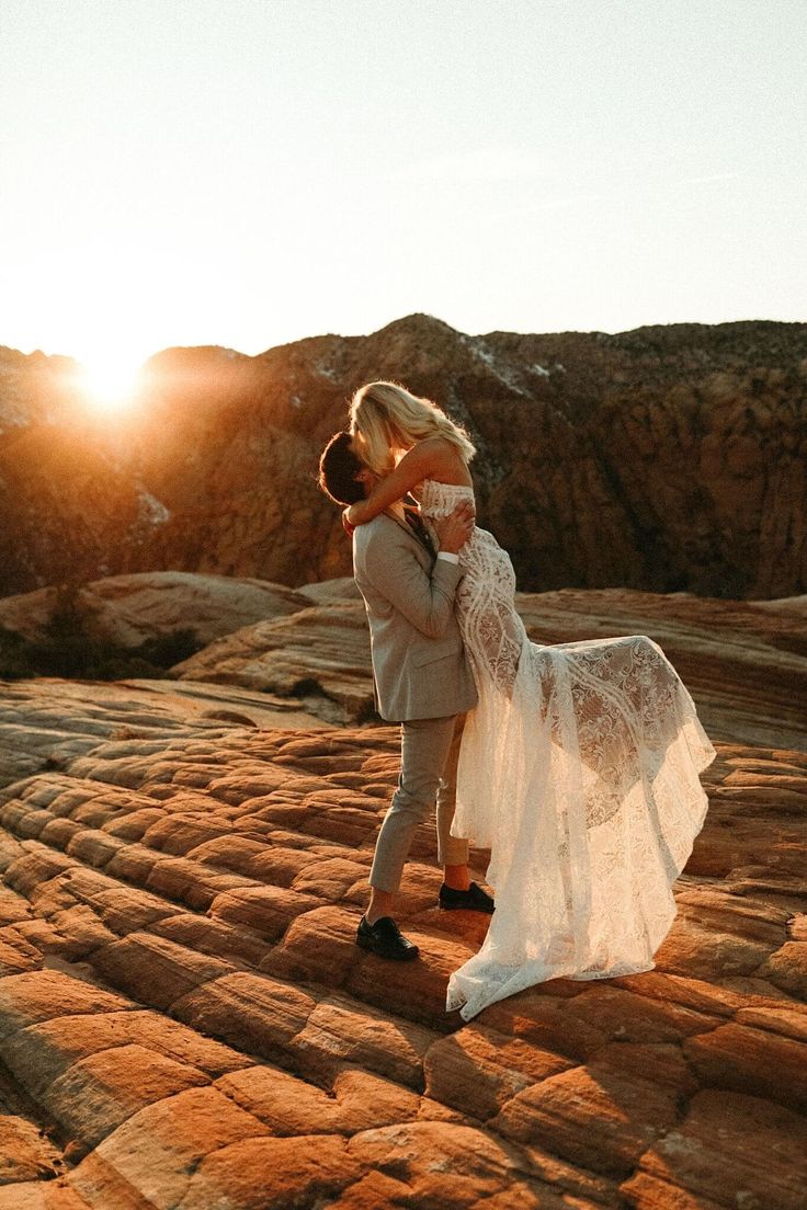 a bride and groom kissing on top of a mountain in the desert at sundown