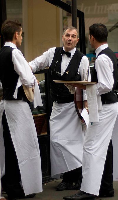 three men in white aprons are standing near each other and one is holding a tray