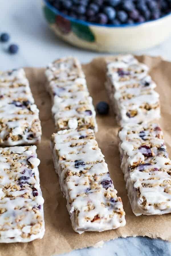 blueberry granola bars are lined up on a piece of parchment paper next to a bowl of blueberries