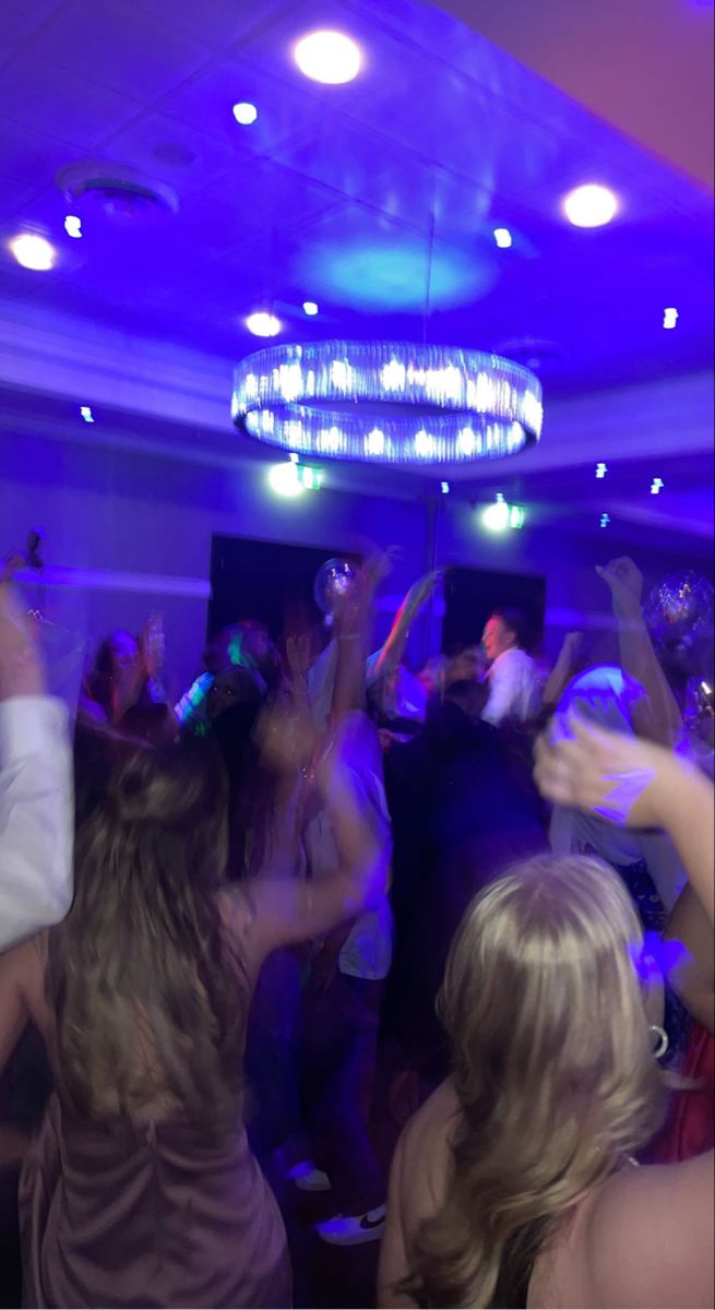 a group of people dancing in a room with blue lights and chandeliers on the ceiling