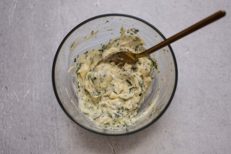 a glass bowl filled with food on top of a white counter next to a wooden spoon