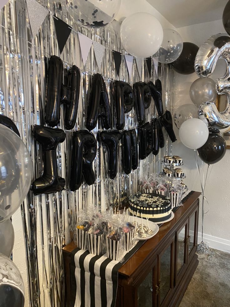 black and white balloons are hanging on the wall next to a table with desserts