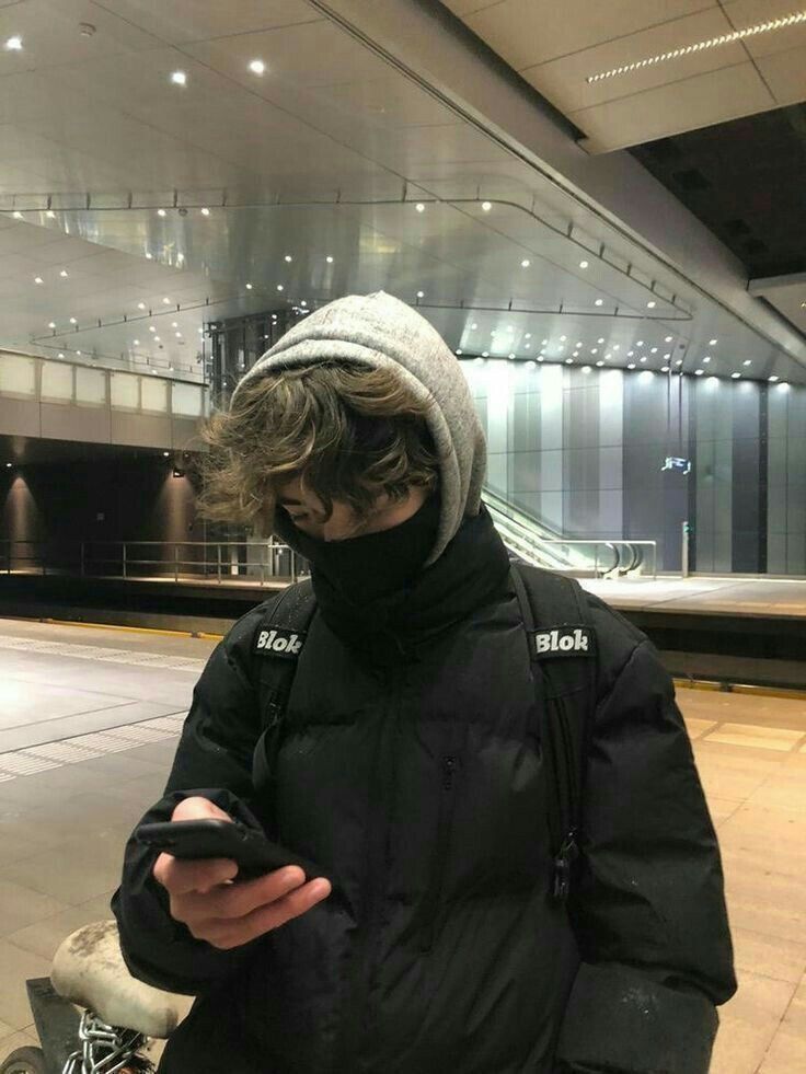 a man wearing a black jacket and hat looking at his cell phone while standing in an airport