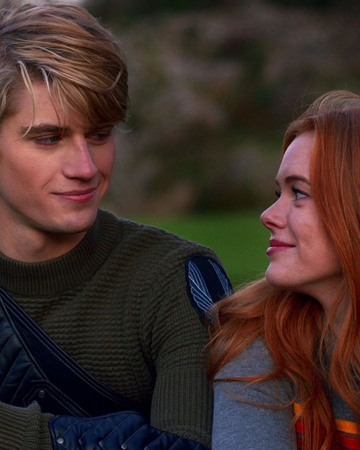 a young man and woman sitting next to each other looking at something in the distance