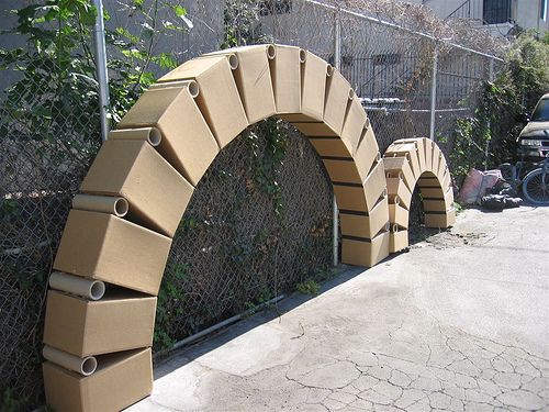 an arch made out of cardboard sitting next to a fence