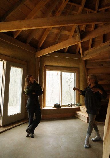 two people standing in an unfinished room looking out the window at another person holding something