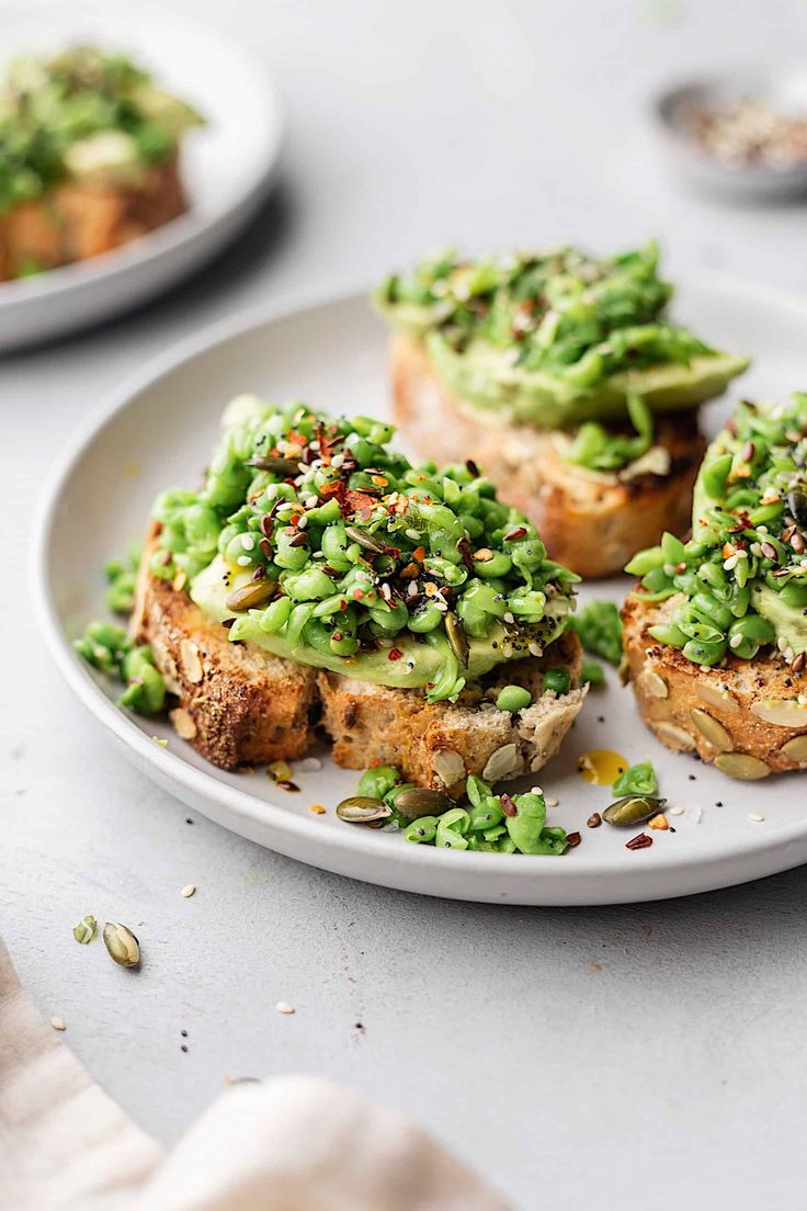 three pieces of bread with green toppings on them sitting on a plate next to other plates