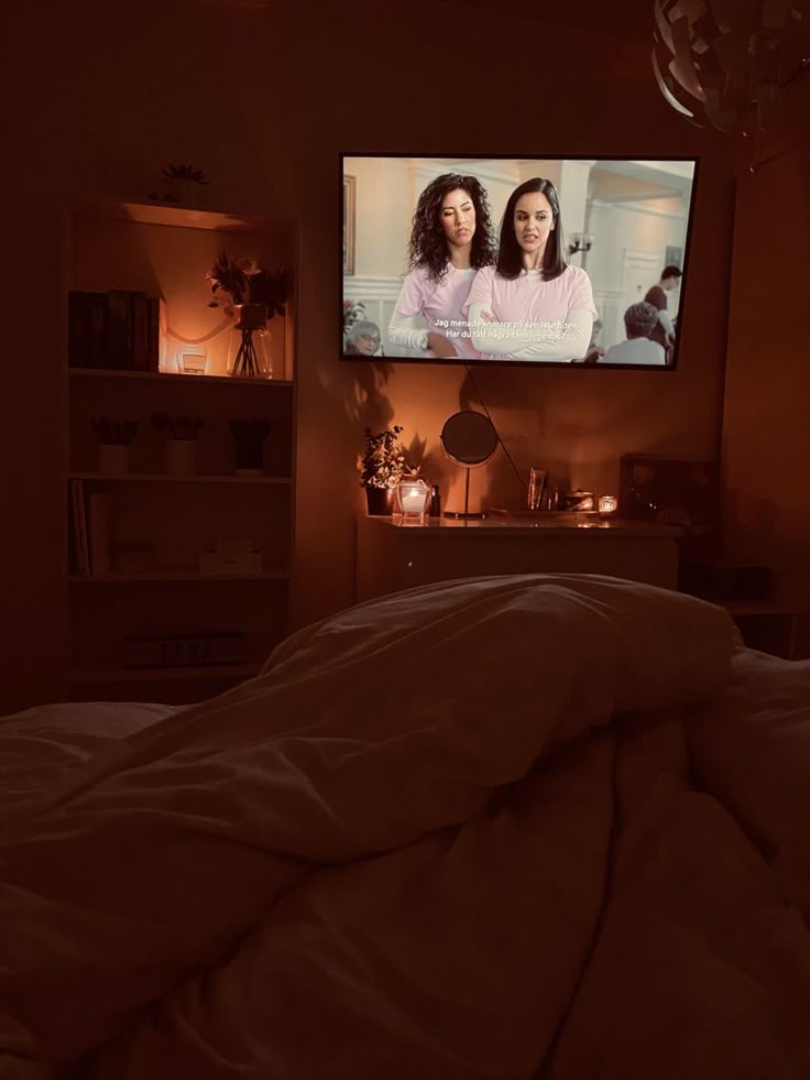 two women are on the television screen in a dark room with white sheets and pillows