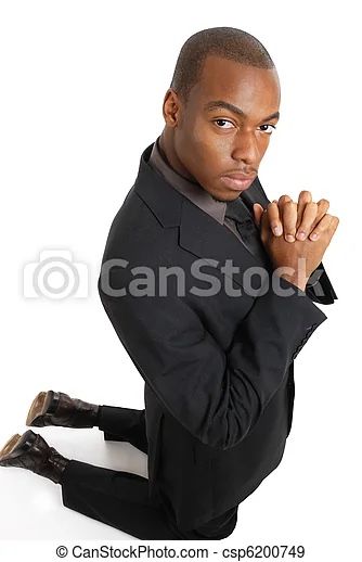 a man in a suit sitting on the ground with his hands clasped to his chest