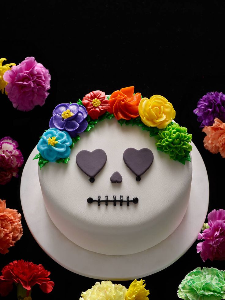 a white cake decorated with colorful flowers and a skull on the top is surrounded by other decorations