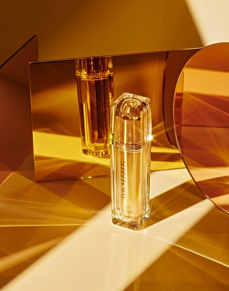 two perfume bottles sitting next to each other on top of a gold tableclothed surface