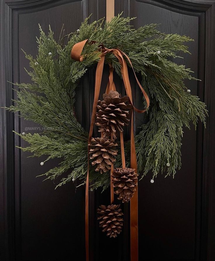 a wreath with pine cones hanging from it's side on a black door frame