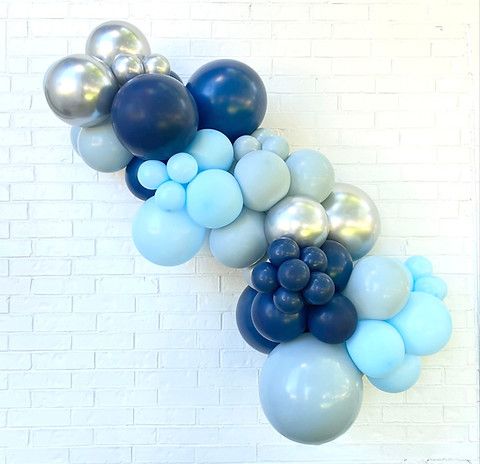 blue and silver balloons are arranged in the shape of an x on a white brick wall