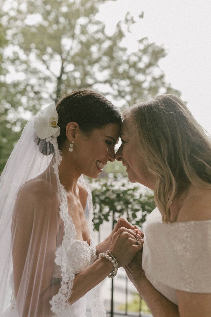 two women in wedding gowns standing next to each other and touching their foreheads