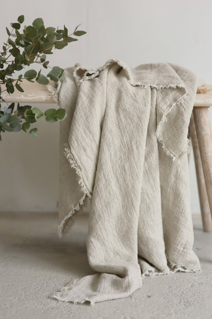 a white blanket sitting on top of a wooden bench next to a potted plant