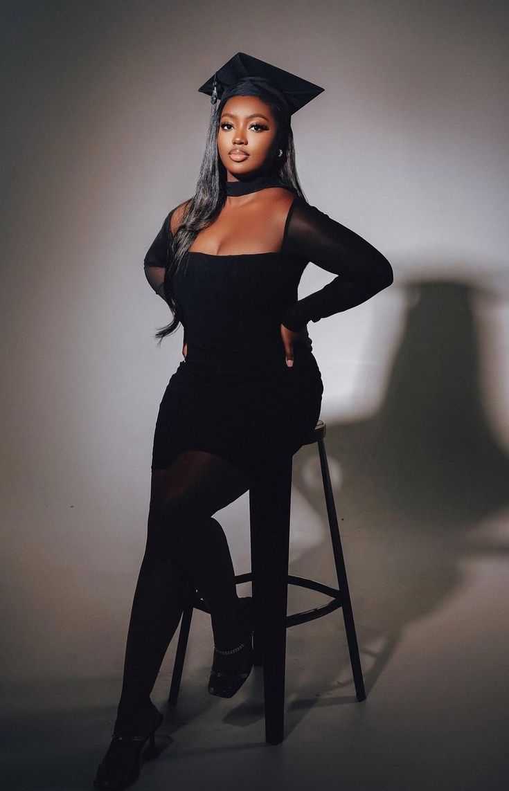 a woman sitting on top of a stool wearing a black graduation cap and gown with sheer sleeves