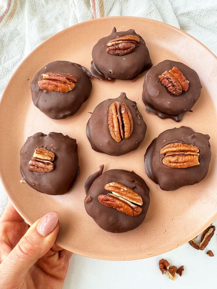 chocolate covered donuts with pecans in the middle on a plate, being held by a person