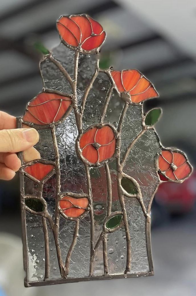 a hand holding up a stained glass piece with red flowers on it and green leaves