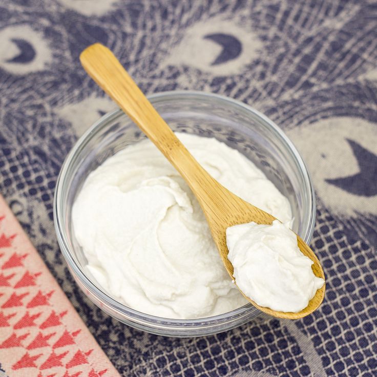 a wooden spoon in a glass bowl filled with whipped cream on top of a table cloth