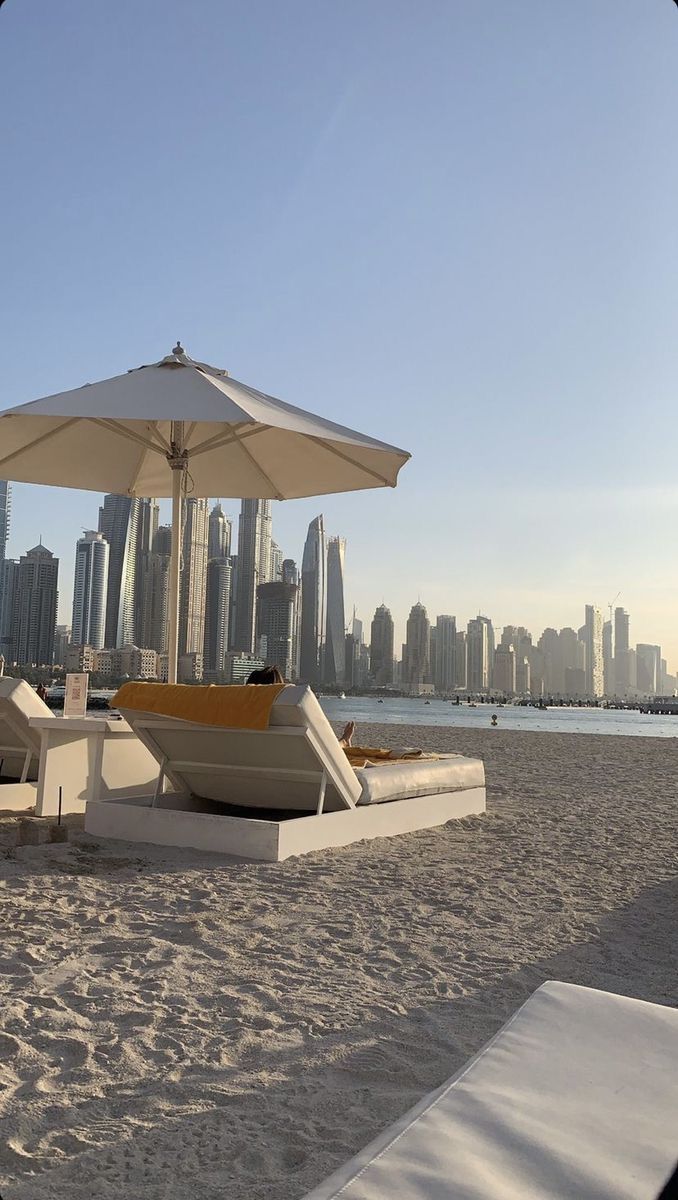 lounge chairs and umbrellas on the beach with city skyline in the backgroud