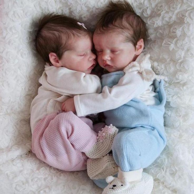 two baby babies cuddle together on a white blanket