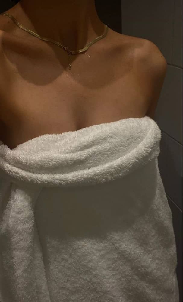 a woman wearing a white towel in the bathroom with her hand wrapped around her neck