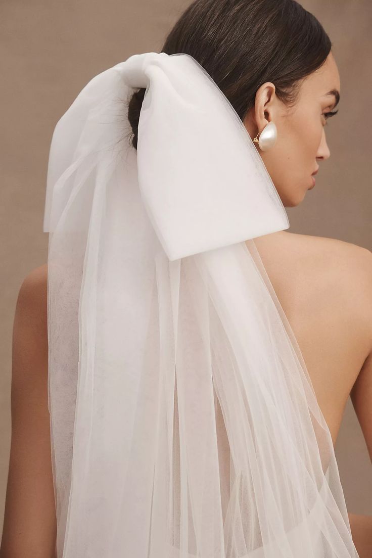 the back of a woman wearing a white veil with an earring on her head